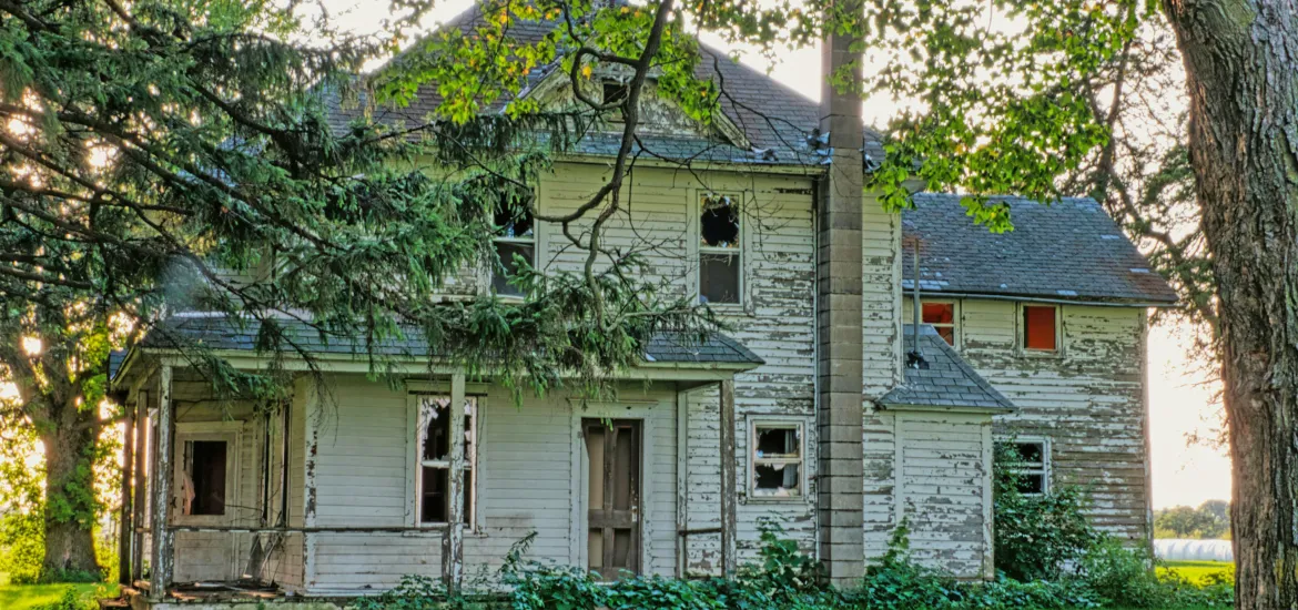 Altes, sanierungsbedürftiges Haus im Grünen – Symbolbild für Förderprogramme zum Kauf und zur Sanierung alter Häuser.