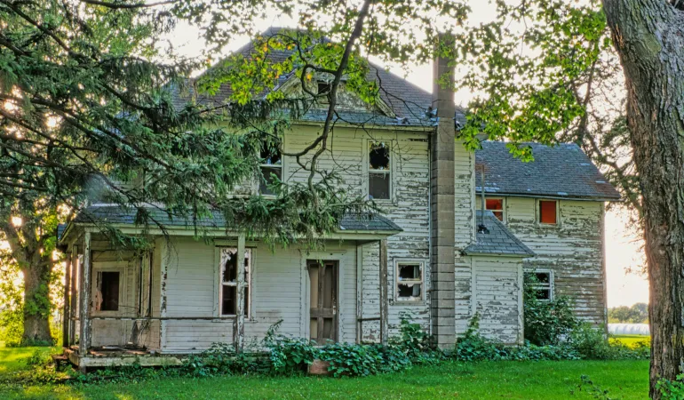 Altes, sanierungsbedürftiges Haus im Grünen – Symbolbild für Förderprogramme zum Kauf und zur Sanierung alter Häuser.